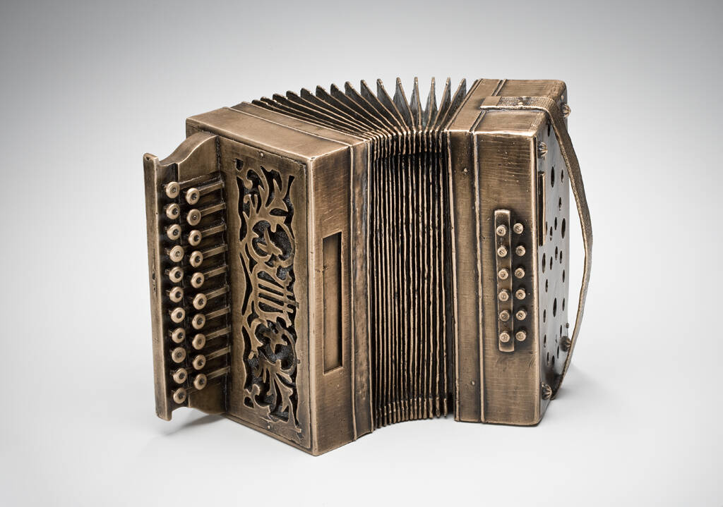 Small accordion made from bronze sitting on its side.